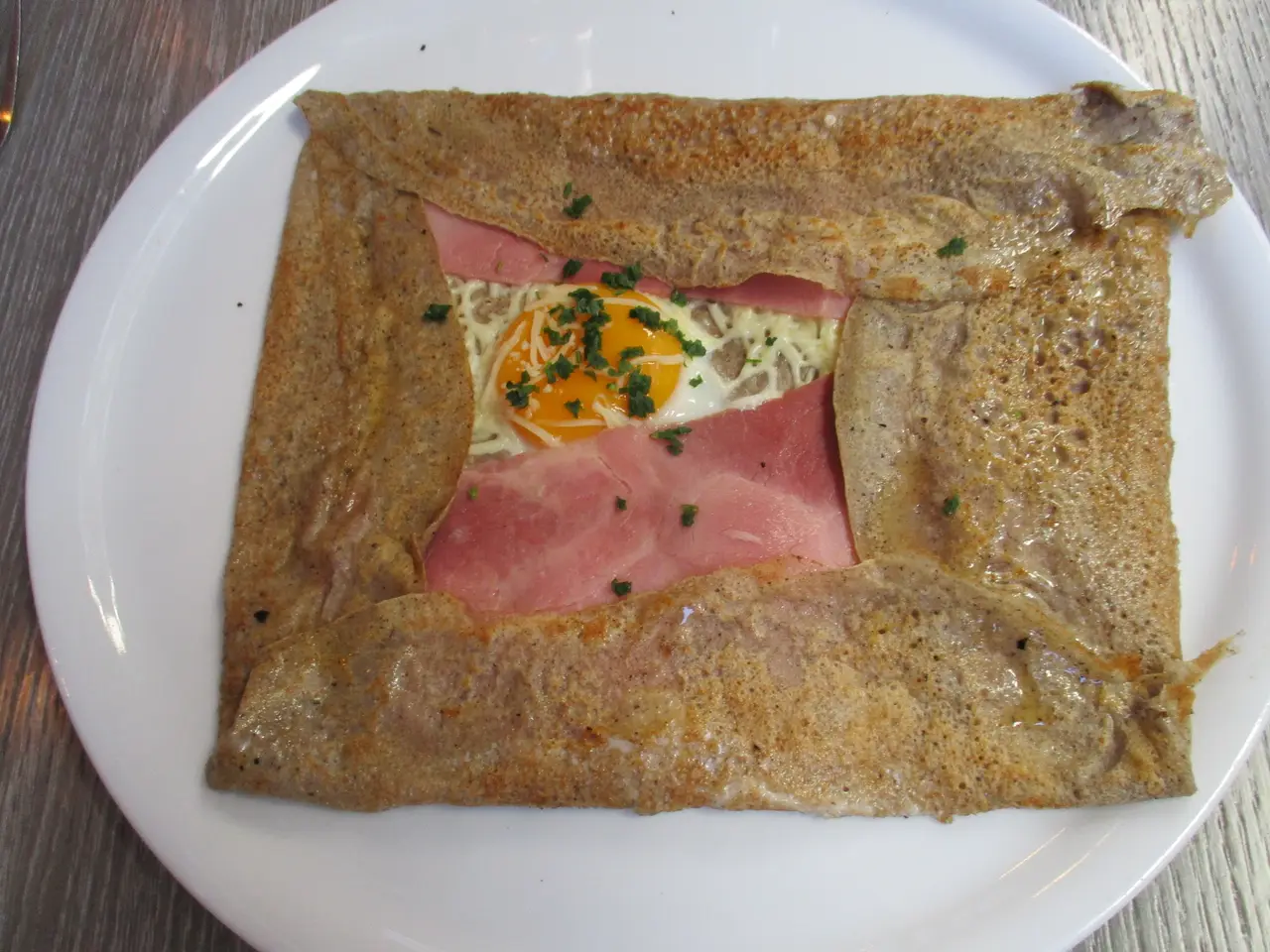 Une galette complète posée sur l'assiette, l'œuf miroir au centre