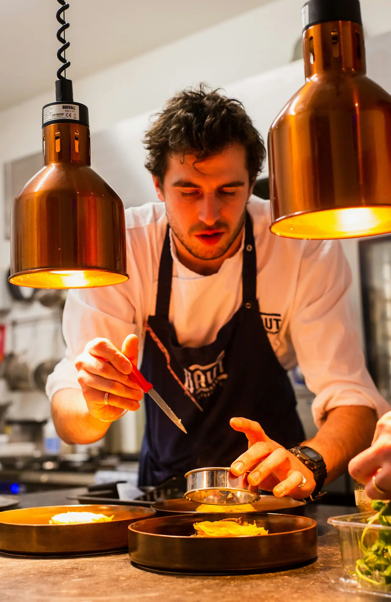 Le chef dresse une assiette à la pince, sous les lampes
